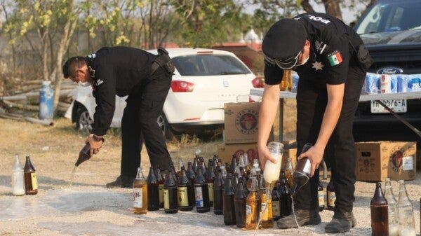 Policías vaciando botellas de cerveza decomisada.
