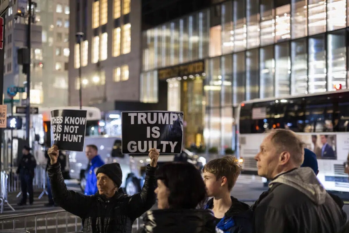 Un manifestante sostiene pancartas contra el expresidente Donald Trump frente a la Torre Trump en Nueva York la noche del lunes 3 de abril de 2023. (AP Foto/Corey Sipkin)