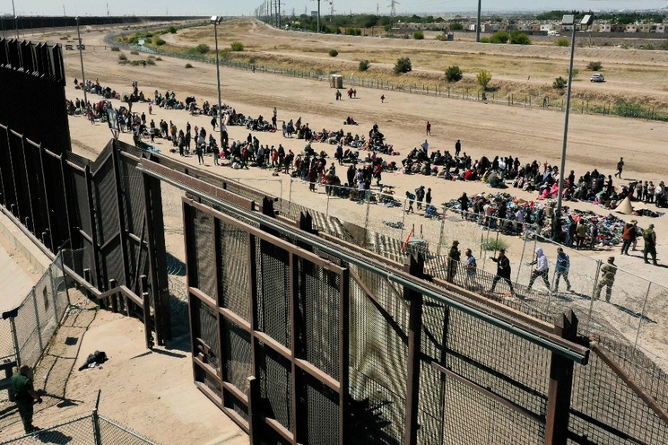 Migrantes esperando a lo largo del muro fronterizo para entregarse a los agentes de la Patrulla Fronteriza de EU para el procesamiento de solicitudes de inmigración y asilo después de cruzar el río Bravo hacia EU en la frontera con México, en El Paso, Texas.